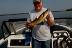 man in white t-shirt holding walleye fish standing on boat in lake